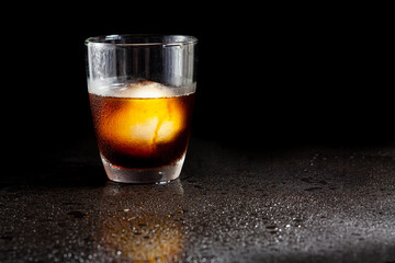 Cold americano decoration with ice ball in whisky glass on a black table.