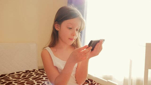 Little girl kid portrait stay at home on a bed use watch smartphone game app and social media videos