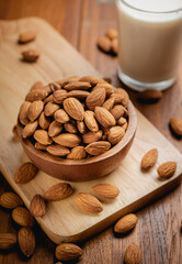 Almond milk in the glass with almond in the wooden bowl on the wooden table.