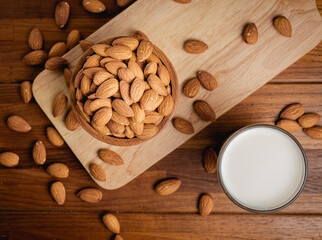 Almond milk in the glass with almond in the wooden bowl on the wooden table.