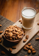 Almond milk in the glass with almond in the wooden bowl on the wooden table.