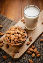 Almond milk in the glass with almond in the wooden bowl on the wooden table.