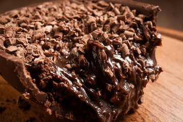 Close up of a cracked stuffed chocolate easter egg with grated chocolate on the top on a wooden stand on a wooden table.