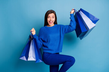 Photo of young happy excited joyful smiling good mood girl holding shopping bags isolated on blue...