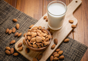 Almond milk in the glass with almond in the wooden bowl on the wooden table.