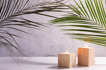 Elegant simple tropical home decor with burning candles in wooden candlesticks with green palm leaf on white wood table, copy space.