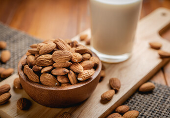 Almond milk in the glass with almond in the wooden bowl on the wooden table.