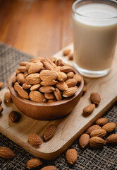Almond milk in the glass with almond in the wooden bowl on the wooden table.
