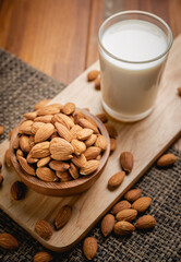 Almond milk in the glass with almond in the wooden bowl on the wooden table.