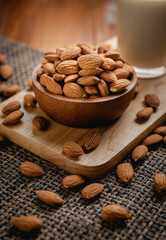 Almond milk in the glass with almond in the wooden bowl on the wooden table.