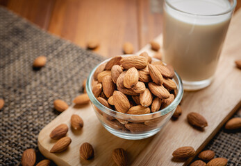 Almond milk in the glass with almond in the glass bowl on the wooden table.