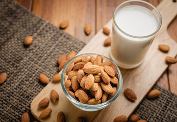 Almond milk in the glass with almond in the glass bowl on the wooden table.