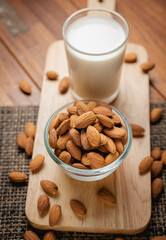 Almond milk in the glass with almond in the glass bowl on the wooden table.