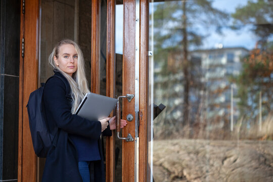 Young woman holding laptop and opening door