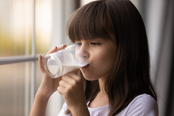 Cute Hispanic little teen girl enjoy tasty delicious healthy dairy drink from glass at home. Small...