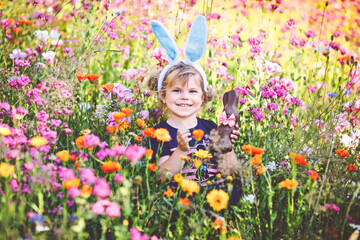 Portriat of adorable, charming toddler girl with Easter bunny ears eating chocolate bunny figure in...
