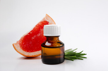 Closeup of glass bottle of aroma oil, juicy grapefruit and rosemary on the white background