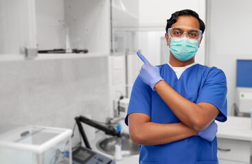 Obraz na płótnie Canvas healthcare, profession and medicine concept - indian doctor or male nurse in blue uniform and face protective medical mask for protection from virus disease over laboratory or hospital background