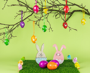 Easter tree branch with decorations, wooden bunny, and painted eggs on the green grass. Holiday composition. 