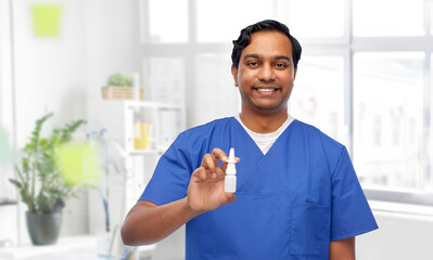 Fototapeta premium medicine, profession and healthcare concept - happy smiling indian doctor or male nurse in blue uniform with nasal spray over medical office at hospital background