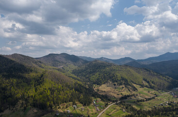 Fototapeta na wymiar Summer mountain landscape, beautiful scenery of Carpathian mountains in Western Ukraine. High mountain peaks, cloudy sky, green forests and a small village at the foot of the hill. Panoramic view.