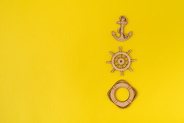 Wooden anchor, steering wheel and lifebuoy on yellow background. Copy space