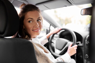 Fototapeta na wymiar safety and people concept - happy smiling young woman or female driver driving car in city