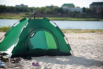 Green tent on river bank against city background. Camping. Leisure