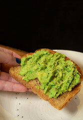 Woman hand taking avocado toast on black background. Healthy eating concept.