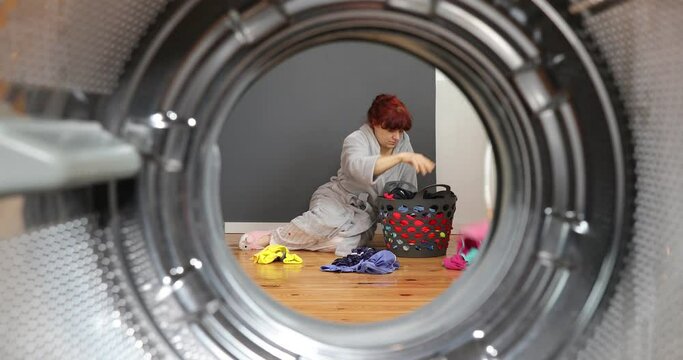 Woman sorting dirty clothes before washing. Housewife sitting with basket and sorting just drying clothes. View Looking Out From Inside Washing Machine.