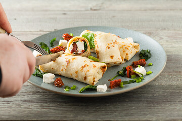 Pancakes with spinach, feta and dried tomatoes. Served on a gray plate. Wooden natural background.