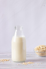 Vegetable oat milk in a glass bottle and oat flakes on a light background. Healthy drinks, vegetarianism. Side view. Vertical photo