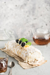 Meringue roll with berry filling on a napkin, with a teapot and a mug of tea on a light background.