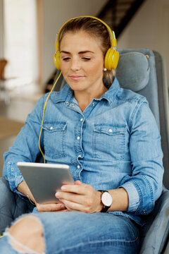 Woman sitting in armchair and using digital tablet