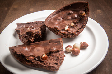 Cracked stuffed chocolate and hazelnut easter egg on a white plate on a wooden table.