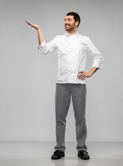 cooking, culinary and people concept - happy smiling male chef in jacket holding something on hand over grey background