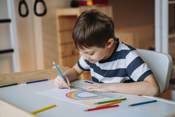 adorable caucasian boy of elementary age drawing with pencils sitting at the desk in his room at home. Image with selective focus