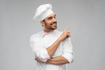cooking, culinary and people concept - happy smiling male chef in toque pointing to something over...