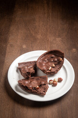 Cracked stuffed chocolate and hazelnut easter egg on a white plate on a wooden table.