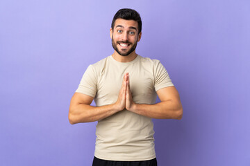 Young handsome man with beard over isolated background keeps palm together. Person asks for something