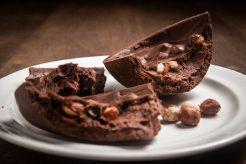 Cracked stuffed chocolate and hazelnut easter egg on a white plate on a wooden table.