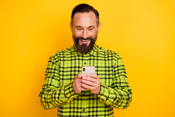 Photo of excited man happy positive smile look read browse smartphone chat type sms isolated over yellow color background