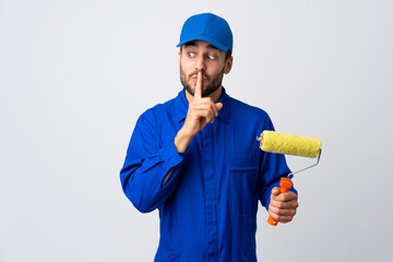 Painter man holding a paint roller isolated on white background showing a sign of silence gesture putting finger in mouth