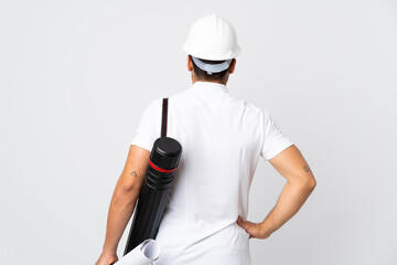 Young architect man with helmet and holding blueprints isolated on white background in back position
