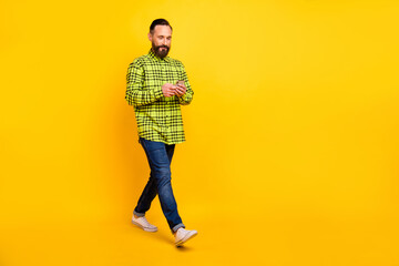 Full size profiles die photo of handsome man happy smile go walk look read browse cellphone isolated over yellow color background