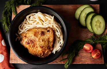 spaghetti with chicken in a black plate on a wooden board with vegetables  top view