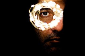 Shallow focus of a person with light garlands around his eye in a dark room