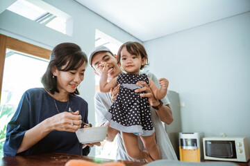 portrait of happy asian father mother and daughter cooking together in modern kitchen