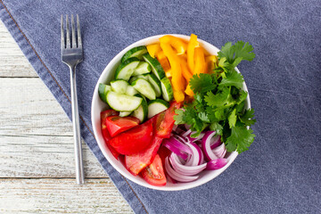 Plate of rainbow salad with different vegetables and herbs in white bowl on white wooden background