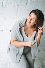 Beautiful happy emotional brunette young woman plus size body positive in comfortable sport wear near the white brick wall